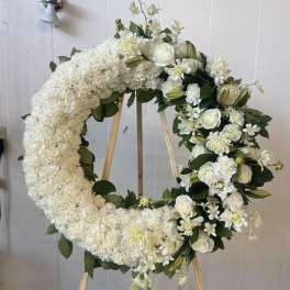 White floral wreath on a wooden easel with roses and lilies