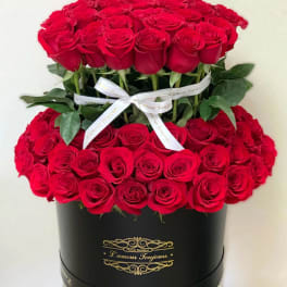 Two-tier arrangement of red roses in a round black hatbox with white ribbon