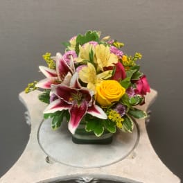 Mixed bouquet with lilies, roses, and small purple flowers in a glass vase
