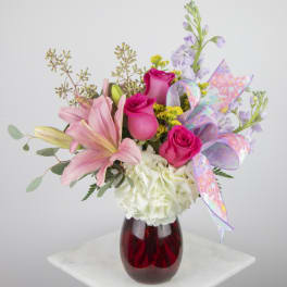 Pink roses and lilies in a red glass vase with a pastel ribbon