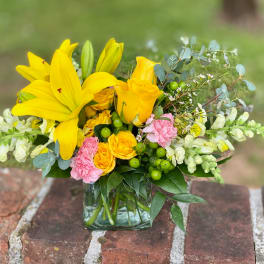 Yellow lilies and roses in a clear glass vase with pink carnations