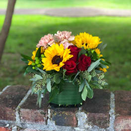 Bouquet of red roses, yellow sunflowers, and pink carnations in a green vase