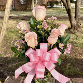 Pink roses and small pink blossoms in a glass vase with a large pink bow