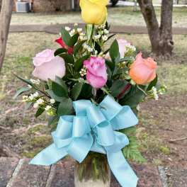Bouquet of multicolored roses in a glass vase with a blue ribbon