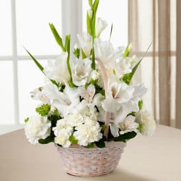 White floral arrangement in a woven basket with pink ribbon handle