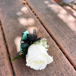 White rose boutonniere with black and teal ribbon on a wooden bench