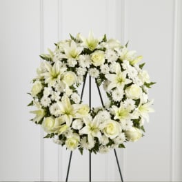White floral wreath on a black stand with lilies and roses