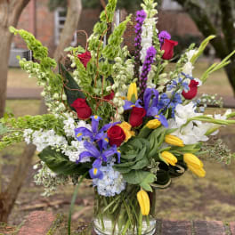Tall mixed bouquet in a clear glass vase with red roses, purple irises, and yellow tulips