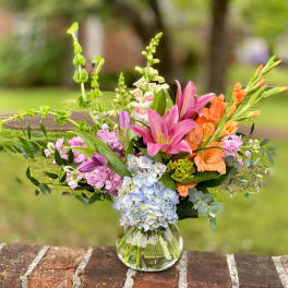 Mixed bouquet of pink, orange, and blue flowers in a glass vase