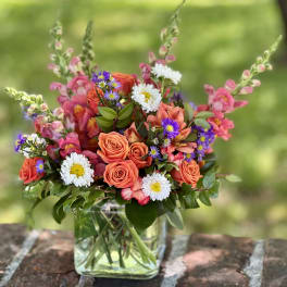 Mixed bouquet of orange roses, pink blooms, and white daisies in a glass vase