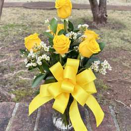 Yellow roses in a clear glass vase with a large yellow ribbon