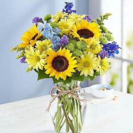 Bouquet of sunflowers, yellow daisies, and blue flowers in a glass vase