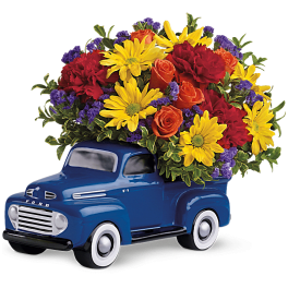 Blue truck-shaped planter filled with red, yellow, and orange flowers