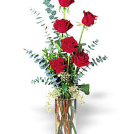 Tall arrangement of red roses in a clear glass cylinder vase with accent foliage