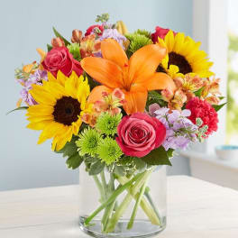 Mixed bouquet with sunflowers, orange lilies, and pink roses in a glass vase