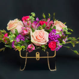 Pink and purple flower arrangement in a black handbag-shaped container