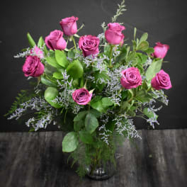 Arrangement of deep pink roses with soft lavender filler flowers in a clear glass vase