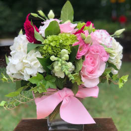 Pink and white flower bouquet in a square glass vase with a pink ribbon