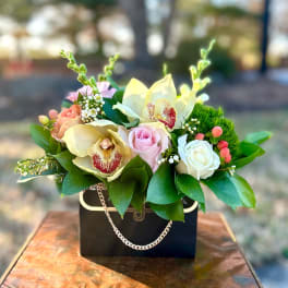 Mixed bouquet with roses and orchids in a black handbag-style container