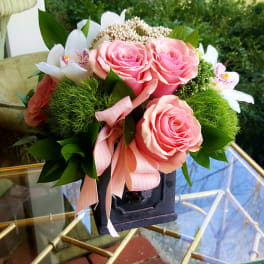 Pink roses and white orchids arranged in a dark vase with a striped ribbon