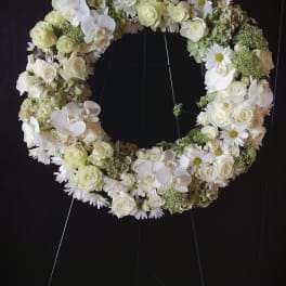 White floral wreath on a stand with roses, orchids, and daisies