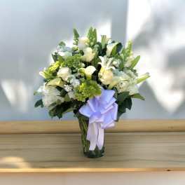 White flowers and green blooms in a glass vase with a lavender ribbon