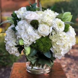 White floral arrangement in a clear glass vase with green accents