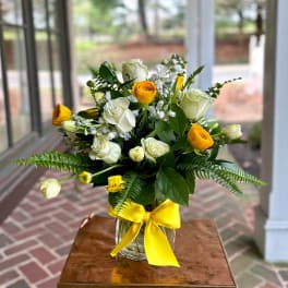Bouquet of white and yellow roses in a glass vase with a yellow ribbon