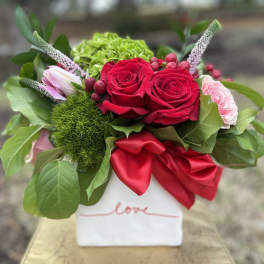 Red roses and pink blooms in a white vase with a red ribbon