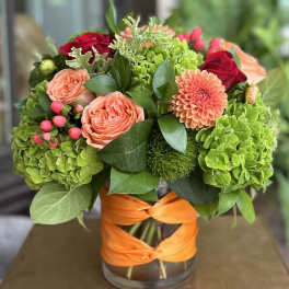 Bouquet of coral roses and green hydrangeas in a glass vase with orange ribbon