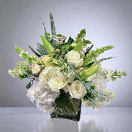 White roses and hydrangeas in a square glass vase with green foliage