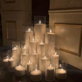Cluster of lit white pillar candles in clear glass cylinders