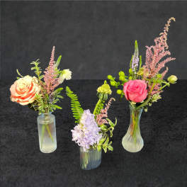 Three small floral arrangements in glass vases with roses and pastel blooms