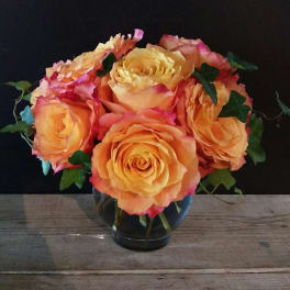 Orange and pink roses arranged in a clear glass vase