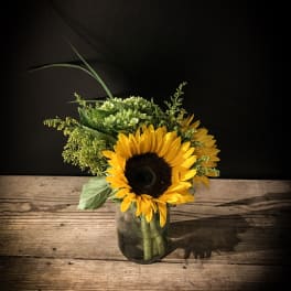 Sunflowers arranged in a glass vase with green filler flowers