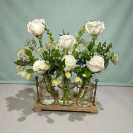 White roses arranged in three glass jars on a wooden holder