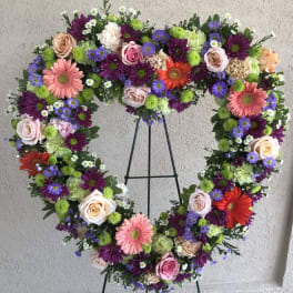 Heart-shaped floral wreath on a black stand with pink, purple, white, and orange flowers
