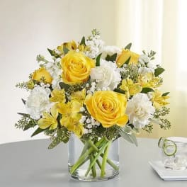 Yellow roses and white flowers arranged in a clear glass vase