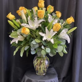 Yellow roses and white lilies arranged in a clear glass vase