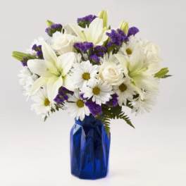 White lilies and daisies with purple filler in a blue vase