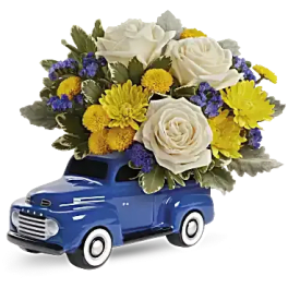 Blue toy truck topped with white roses and yellow flowers