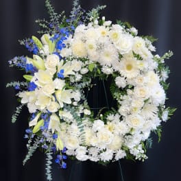 White floral wreath with blue accents on a stand