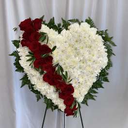 Heart-shaped floral tribute with red roses and white flowers on an easel