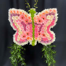Butterfly-shaped floral arrangement with pink and peach blooms and trailing greenery