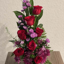 Red roses and purple flowers in a clear glass vase