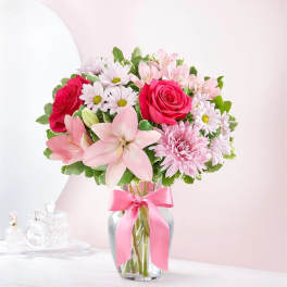 Pink and white mixed flower bouquet in a glass vase with a pink ribbon