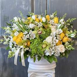 White and yellow floral arrangement in a white urn vase