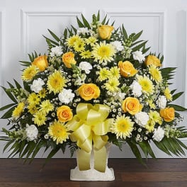 Yellow and white floral spray with a ribbon on a pedestal stand