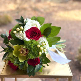 Hand-tied bouquet with red roses, white hydrangeas, green cymbidium orchid, and green dianthus tied with white ribbon