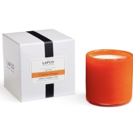 Orange candle in a glass jar beside a white gift box